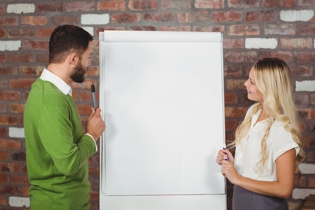 A manager giving feedback to an employee in a one-on-one setting, with a visible whiteboard in the background listing goals and objectives. The employee seems engaged and inspired during the feedback session. The manager gestures towards the goals, emphasizing the path forward.