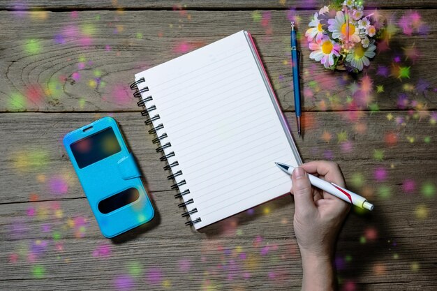A person writing in a physical planner at a desk, with various colored pens and sticky notes around. The planner is open to a page showing a time-blocked schedule.