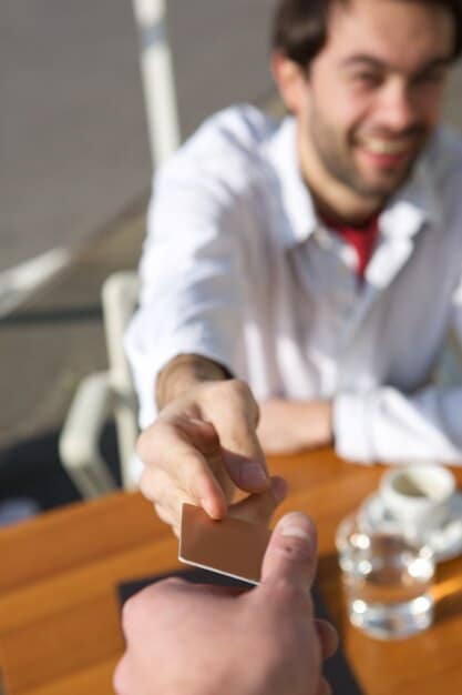 A close-up shot of two professionals exchanging business cards and smiling during a conference break, with blurred attendees in the background.