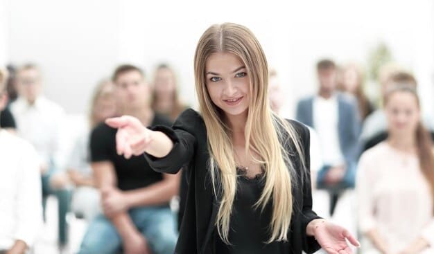 A person confidently extending their hand for a handshake while making eye contact, set against a blurred backdrop of a conference hall full of people.