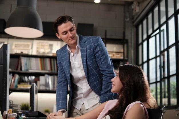 A successful professional woman mentoring a young professional man in a modern office setting, both looking engaged and focused.
